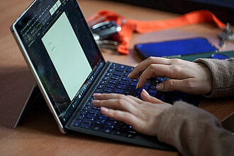 Zwei Hände tippen auf der Tastatur eines Laptops.