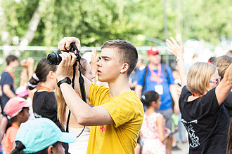 Ein junger Mann fotografiert in eine Menschenmenge.
