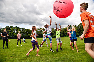 [Translate to Leichte Sprache:] Kinder spielen auf einer Wiese mit einem Ball. 