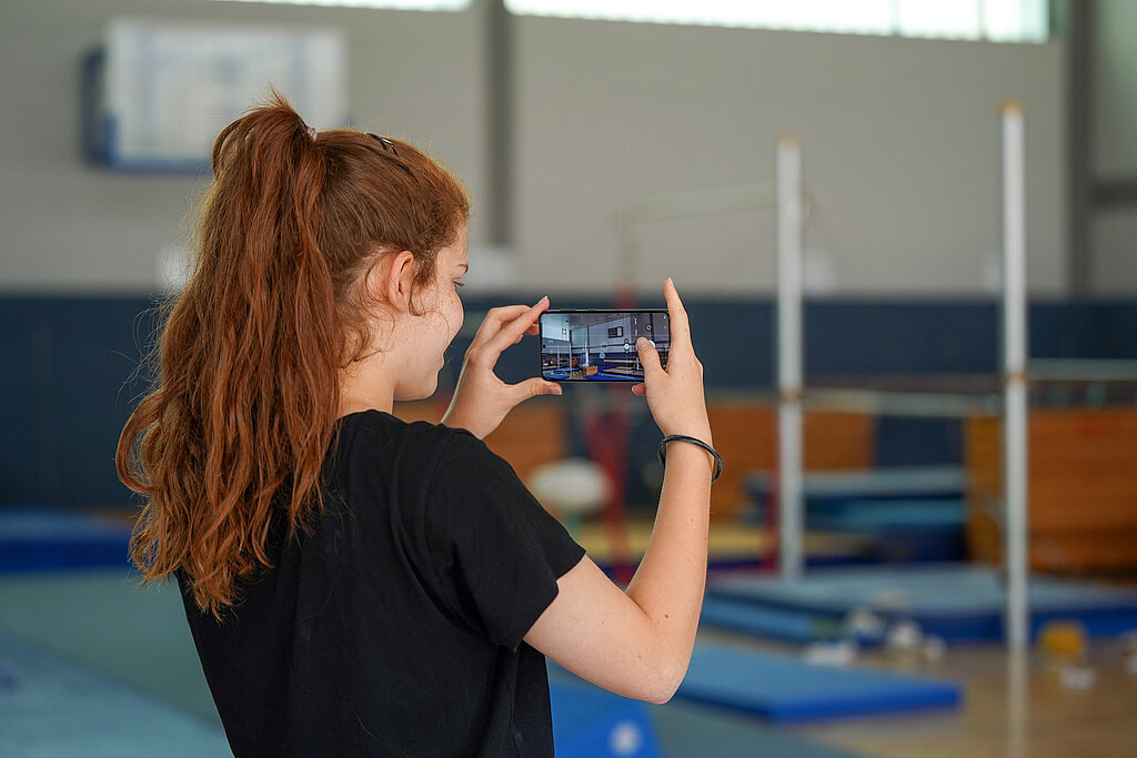 Ein Mädchen filmt mit einem Handy die Turnhalle.