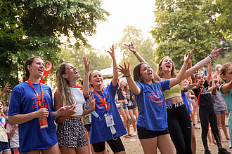 Junge Mädchen tanzen und singen gemeinsam auf einer Festwiese.