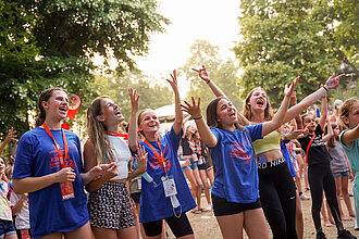 Junge Mädchen tanzen und singen gemeinsam auf einer Festwiese.