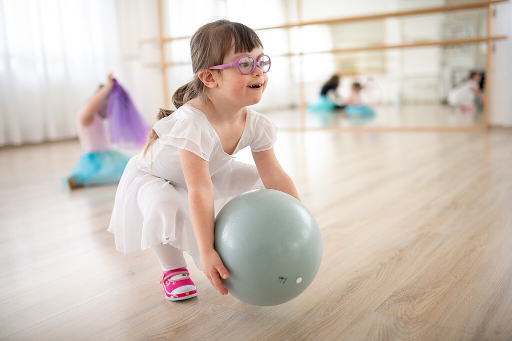 Ein Mädchen mit Brille hebt einen Ball auf.