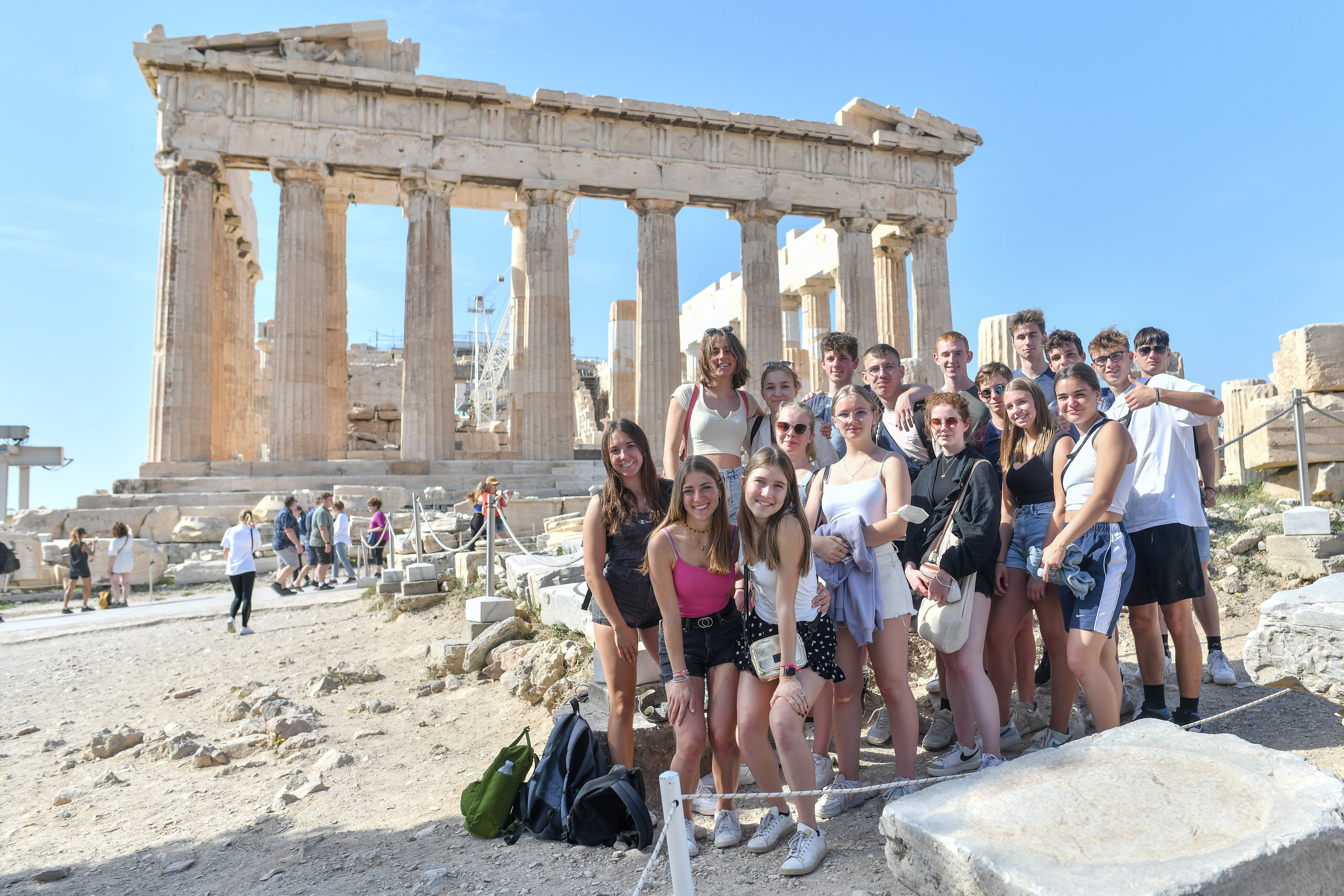 Eine Gruppe junger Menschen steht vor einem antiken Gebäude in Griechenland und lacht in die Kamera.