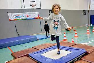 Ein Mädchen turnt auf einem Trampolin.