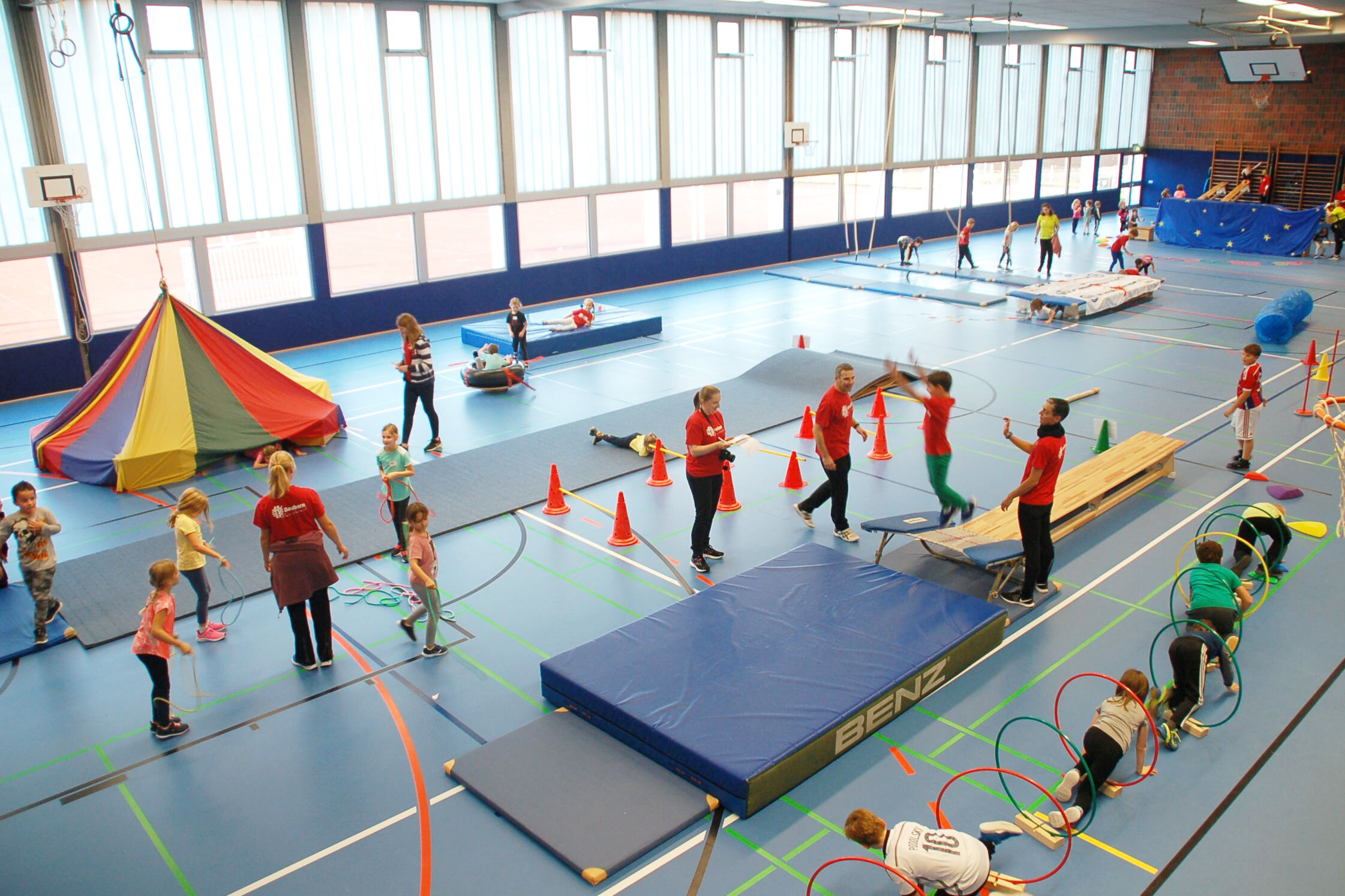 Kinder spielen in einer Halle mit vielen Spiel- und Sportgeräten.