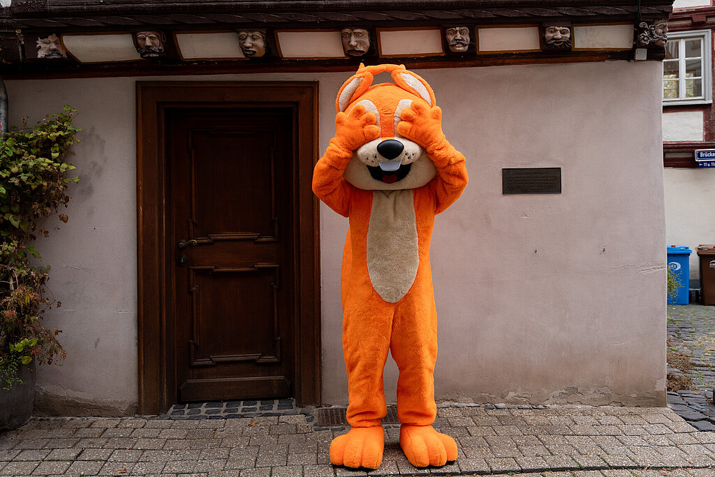 Das Maskottchen der hessischen Turnjugend steht vor dem Haus der sieben Laster in Limburg und hält sich die Augen zu.