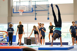 Kind durchläuft im Handstand einen Parkour aus Geräten in der Halle.