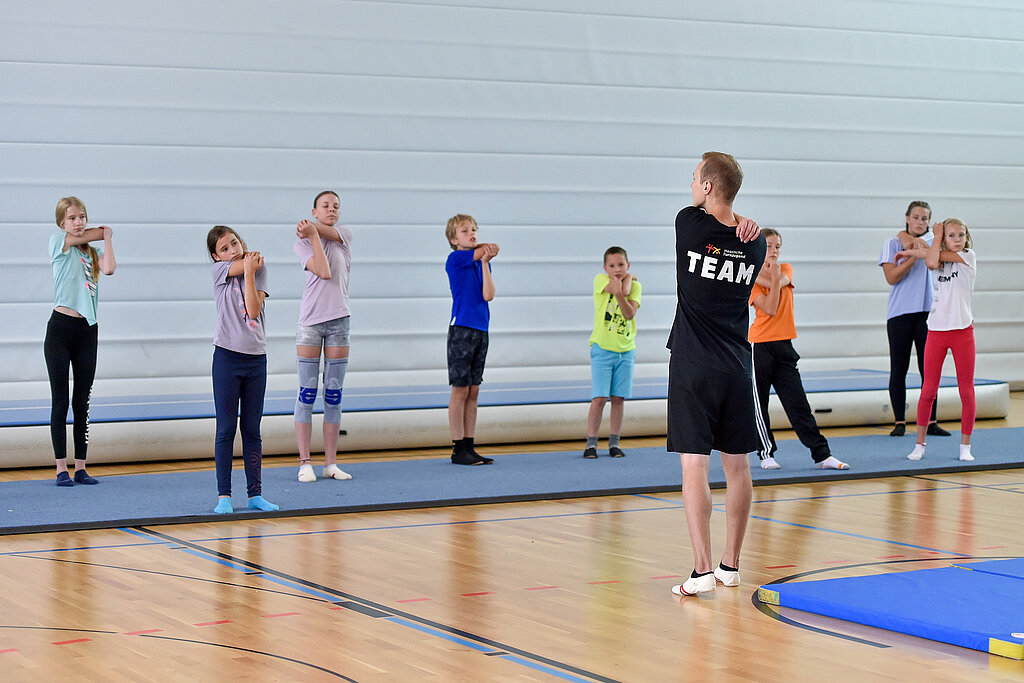 Ein Mann macht mit Kindern eine Dehnübung in der Sporthalle.