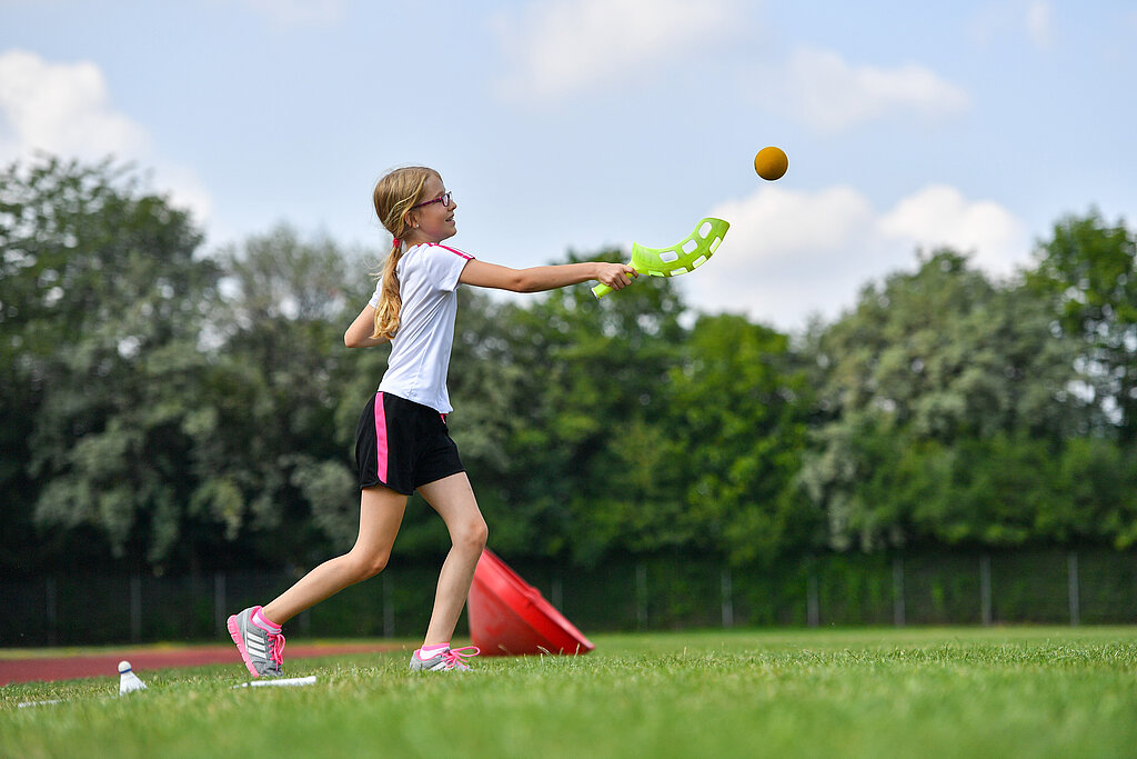 Mädchen spielt draußen mit einem Köcher und Ball.