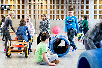 Kinder spielen in der Turnhalle mit verschiedenen Geräten.