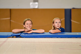 [Translate to Einfache Sprache:] Zwei Kinder lehnen am Trampolin und lachen. 