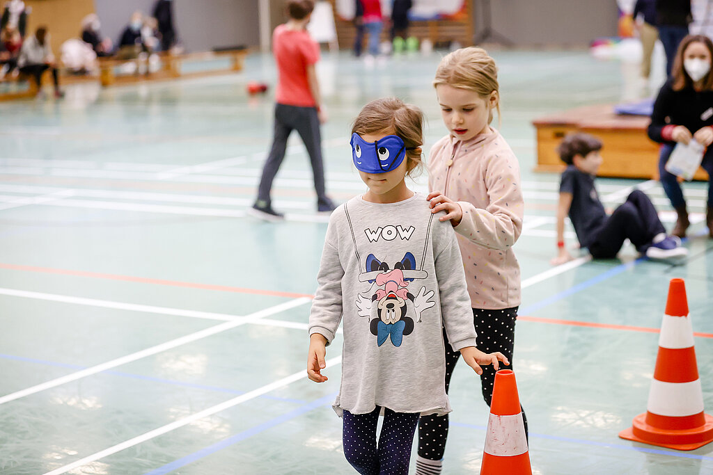 Zwei Kinder führen sich blind durch einen Parkour.