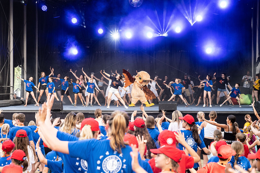 Vor und auf einer Bühne tanzen viele Menschen.