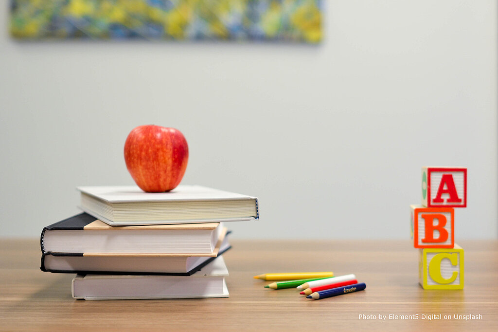 Bücher, ein Apfel und ABC-Würfel auf einem Schreibtisch.