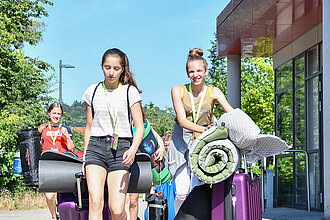 Zwei Mädchen reisen mit Koffern zum Turnfest an. 
