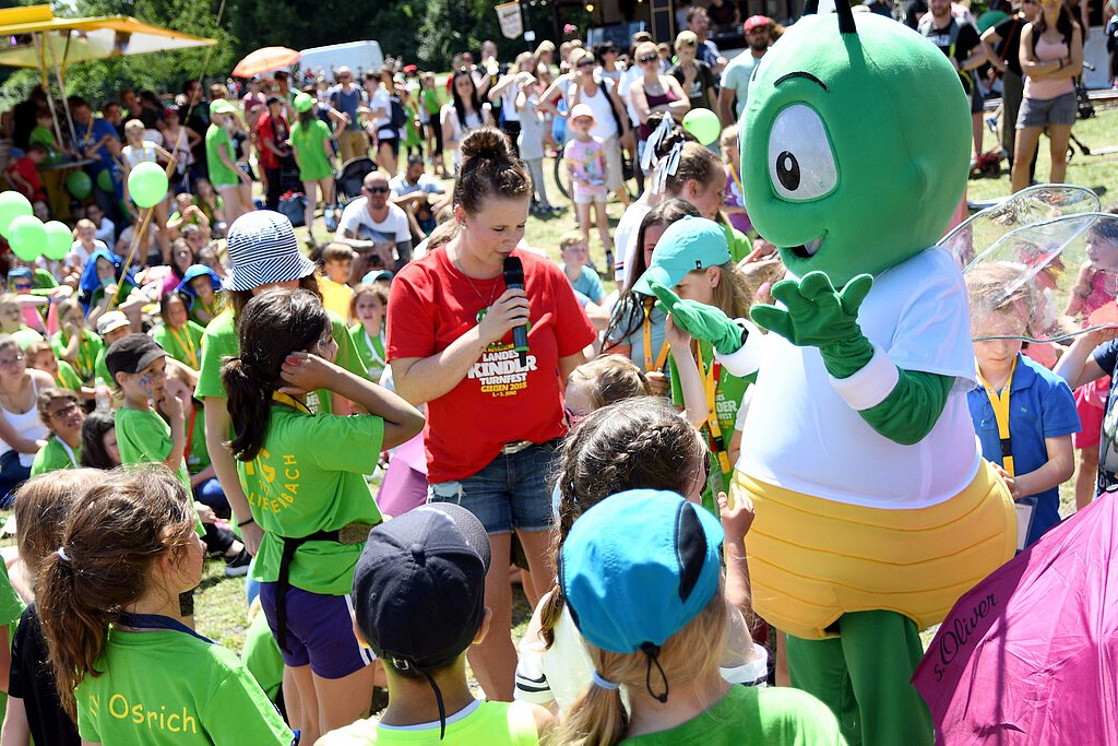 Das Maskottchen des letzten Landeskinderturnfestes umringt von Kindern.