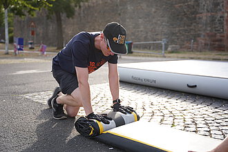 Eine Person in Arbeitskleidung und Turnfest-Design rollt eine Plane zusammen.