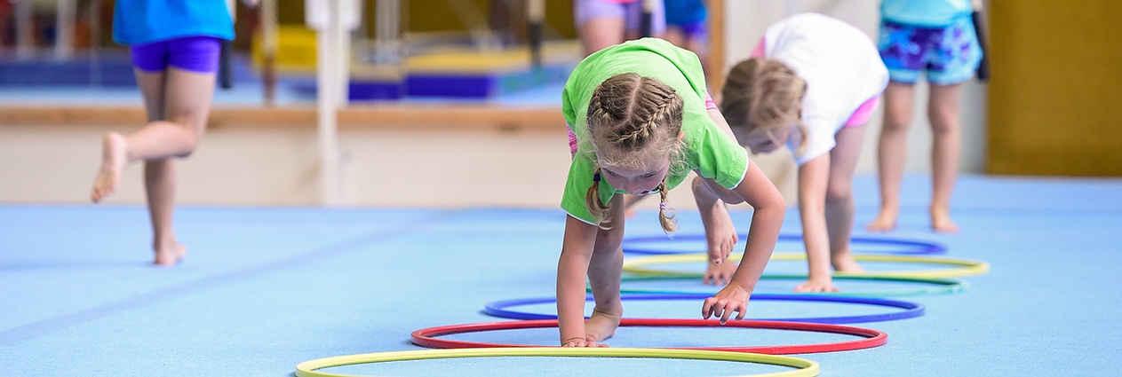 Kinder krabbeln durch Reifen die auf dem Boden einer Sporthalle liegen