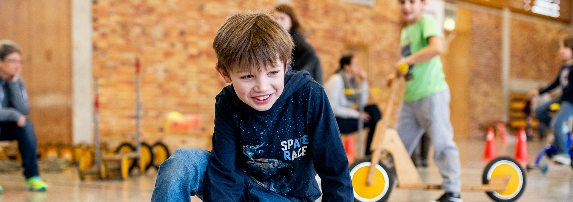 Viele Kinder spielen mit kleinen Turngeräten in einer Halle.