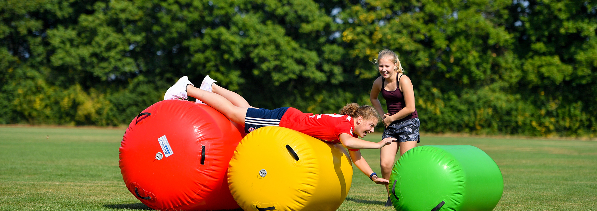 Zwei Mädchen turnen draußen auf zwei Turngeräten und lachen.