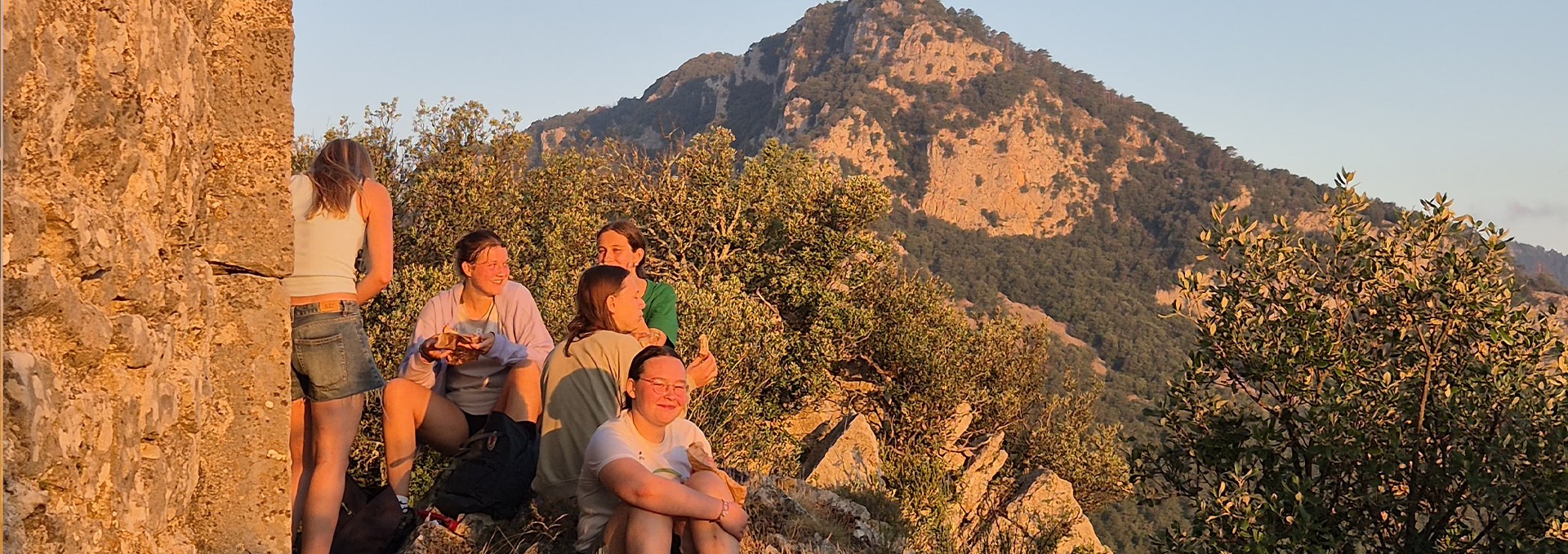 Jugendliche sitzen auf einem Felsen bei Sonnenuntergang.