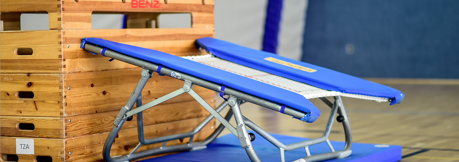 Ein Mini-Trampolin steht vor einem großen Kasten in einer Sporthalle.