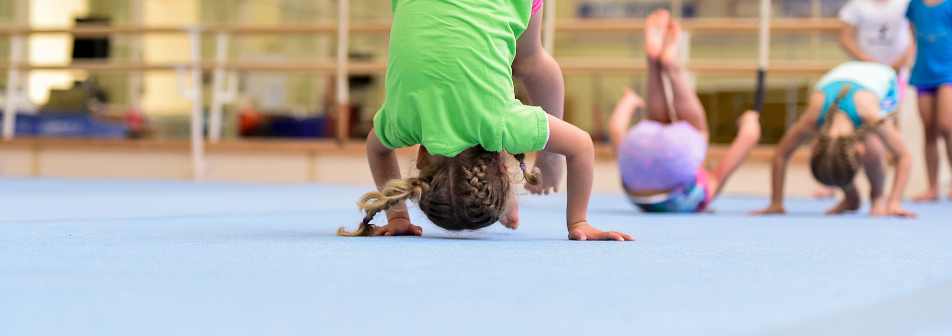 Viele Kinder machen eine rolle Vorwärts in einer Sporthalle.