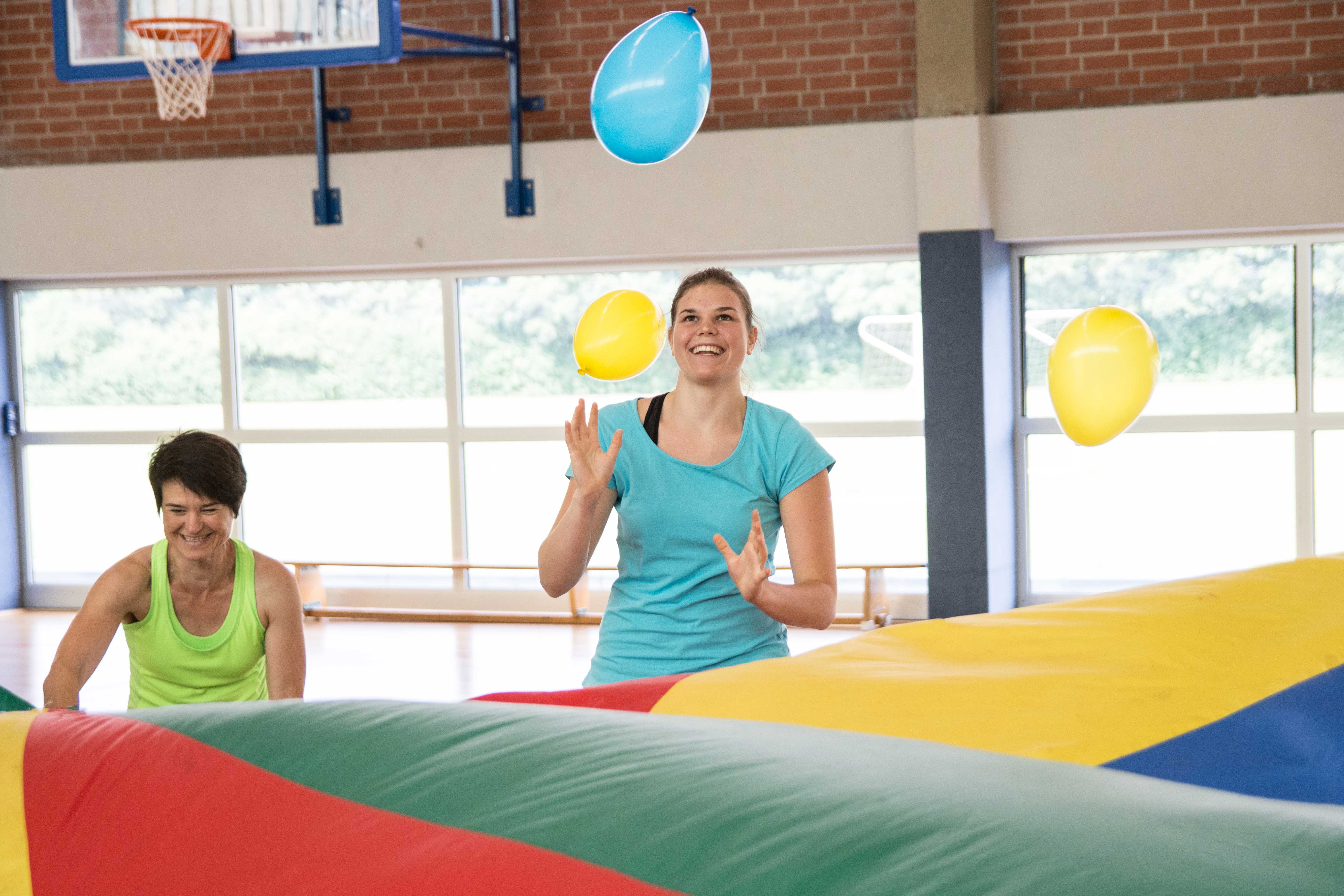 Zwei Übungsleiterinnen testen ein Schwungtuch mit Luftballons.