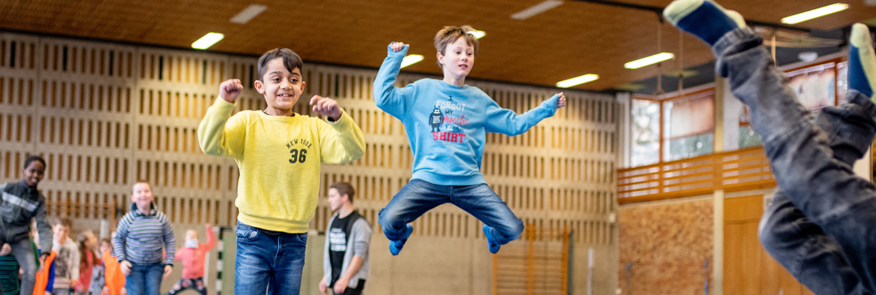 Mehrere Kinder toben in einer Sporthalle.