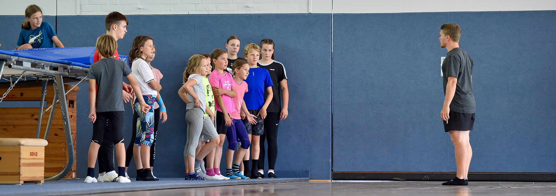 Ein Übungsleiter spricht mit Kindern vor einem Trampolin.
