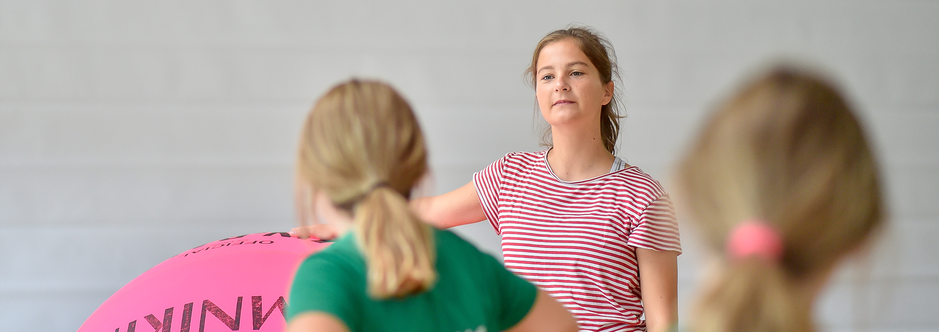 Junge Frau lehnt an großem Ball und spricht zu Kindern.